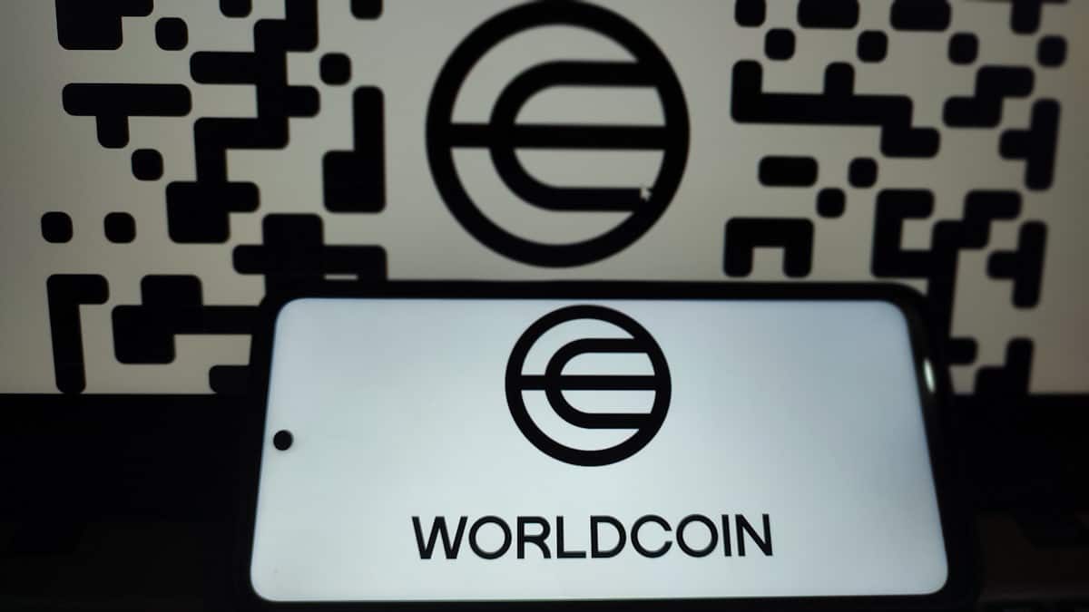 Logomarca da Worldcoin em tela de celular e no fundo