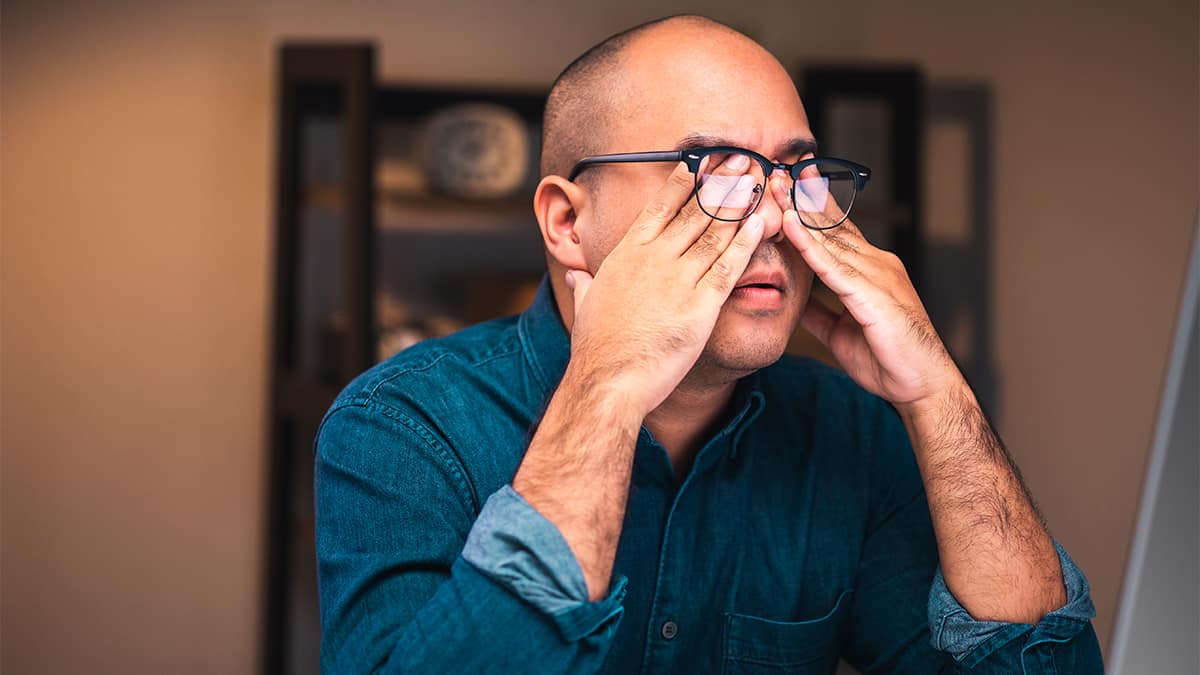 Homem apertando os olhos por trás dos óculos por conta do cansaço