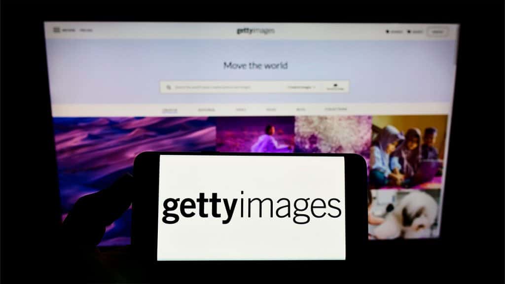 Pessoa segurando celular com logotipo do Getty Images na tela e o site aberto no fundo num computador