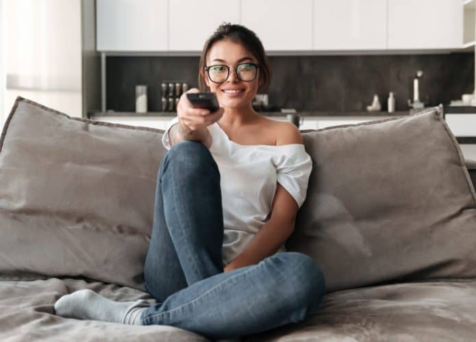 jovem-feliz-sentado-no-sofa-em-casa-assistir-tv-695x500