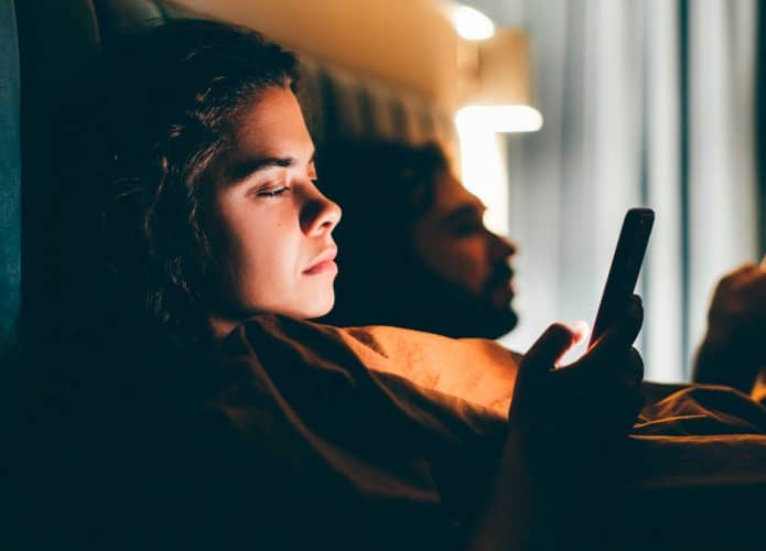 Casal deitado na cama usando celular
