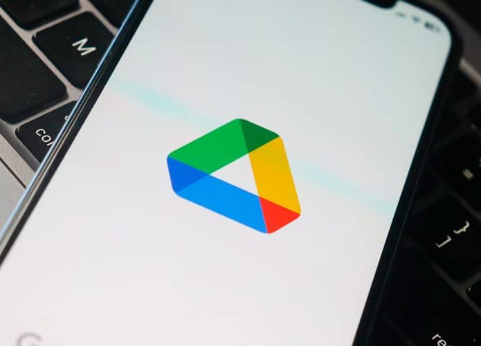 Logotipo do Google Drive no aplicativo aberto num iPhone sobre um Macbook