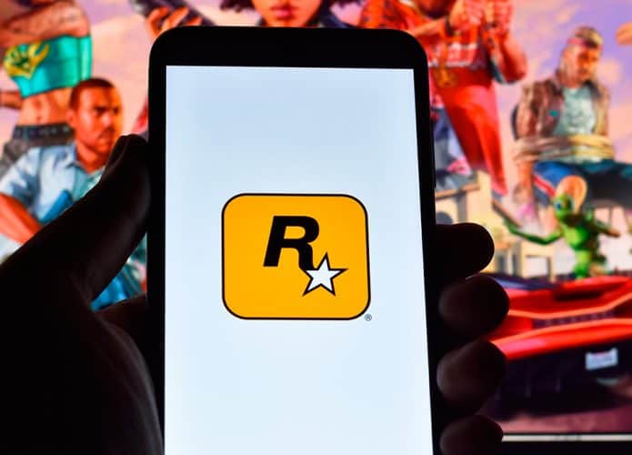 Celular com logotipo da Rockstar na frente de monitor com pôster de GTA