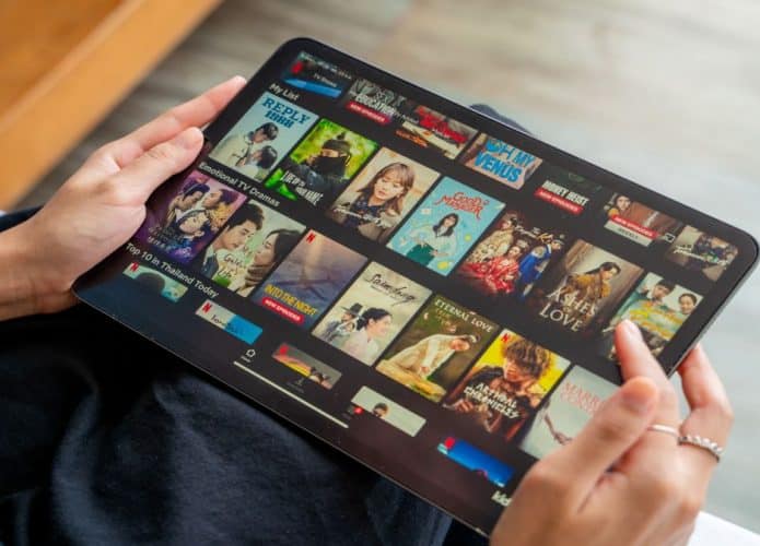 Pessoa segurando um tablet com imagem de tela em streaming com muitos doramas