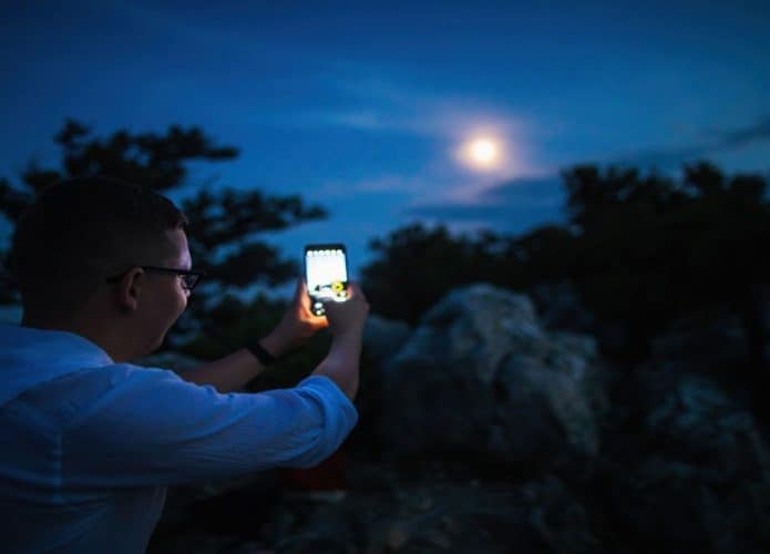 Pessoa tirando foto da lua com celular no escuro