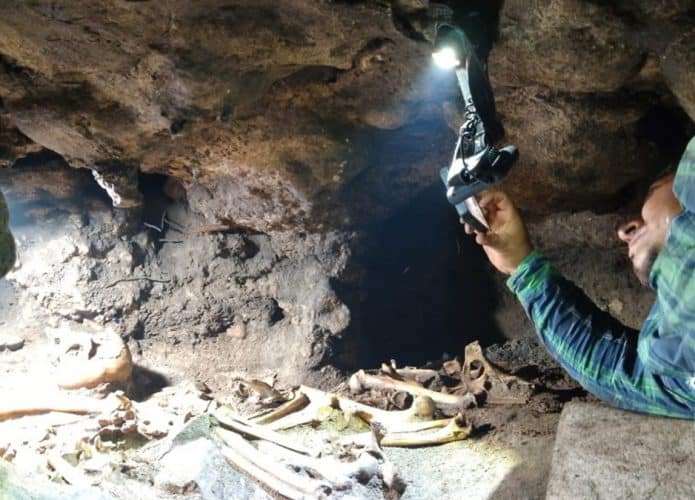Arqueólogo tirando foto de restos mortais em caverna