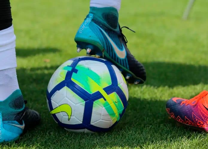 Jogador de futebol com pé em cima de bola sobre campo