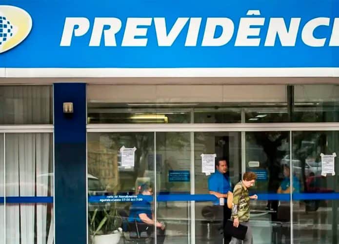 Idosa passando pela fachada de agência do INSS