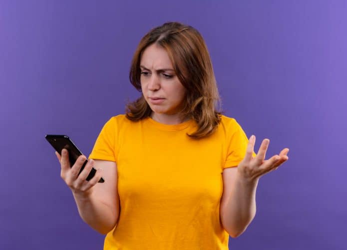 confused-young-casual-woman-holding-mobile-phone-showing-empty-hand-looking-it-isolated-purple-space-695x500