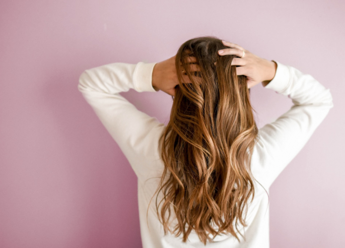 imagem mostra mulher de costas para a câmera e coçando o cabelo longo com a ponta dos dedos