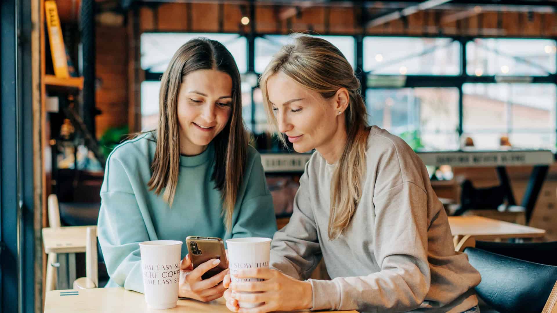 Duas mulheres na cafeteria olhando o celular