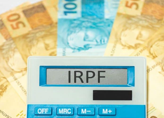 cédulas de 100,00 e 50,00 de fundo e calculadora com a sigla IRPF na tela de digitação