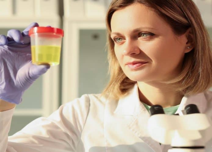 Cientista mulher loira de cabelo curto com olhos claros, segurando um pote de urina amarela