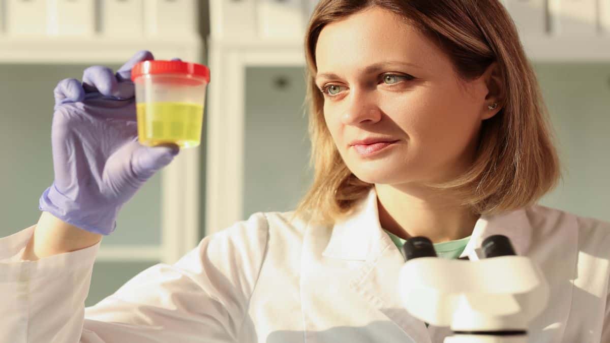 Cientista mulher loira de cabelo curto com olhos claros, segurando um pote de urina amarela