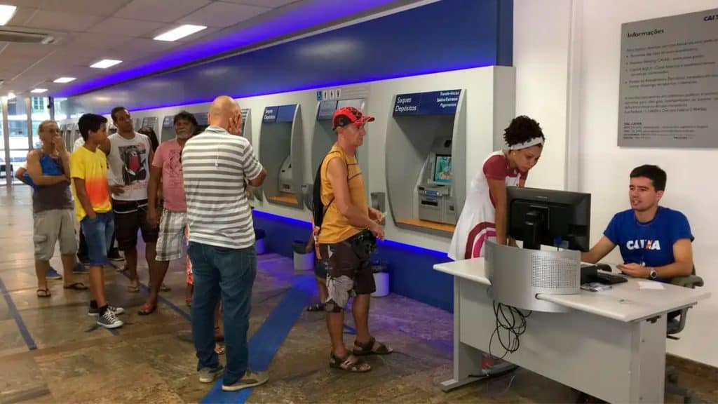 Pessoas em fila de caixa eletrônico na Caixa Econômica Federal