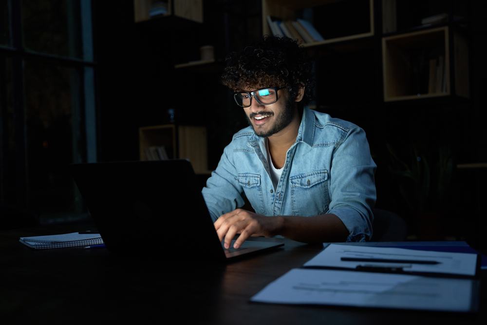 homem trabalhando a noite com notebook e sorrindo