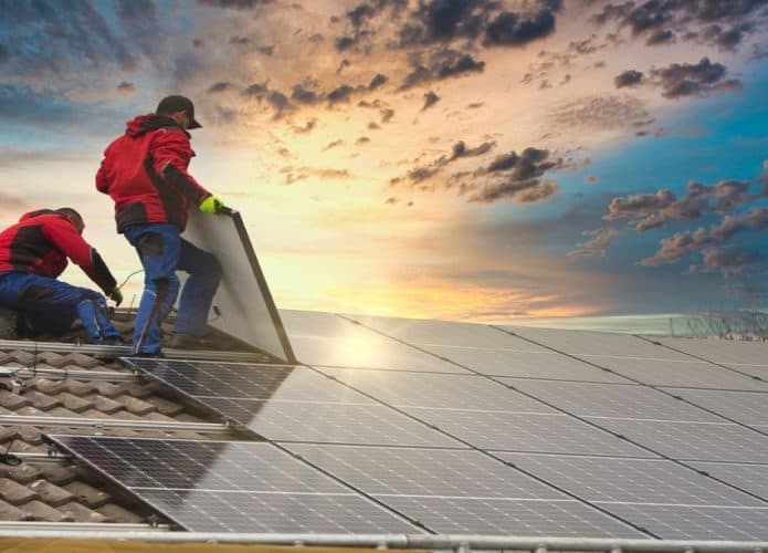 Dois homens com uniformes iguais colocando painel solar em um teto alto