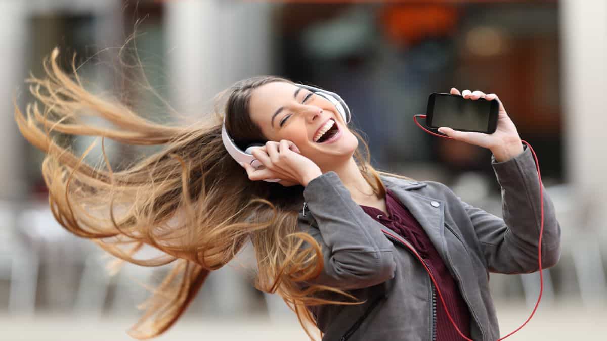 mulher jovem sorrindo com fone de ouvido e celular na mão