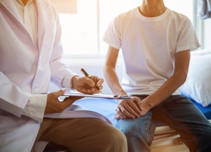 imagem mostra um médico de jaleco atendendo um paciente dentro de um quarto de hospital