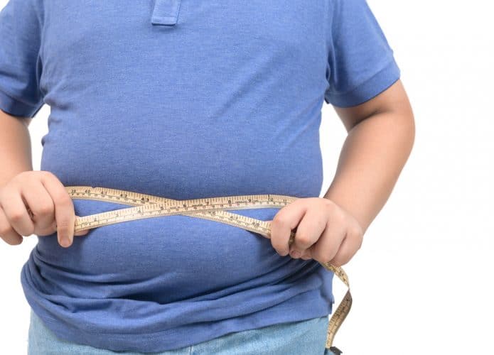 Pessoa obesa transpassando uma fita métrica por sua barriga