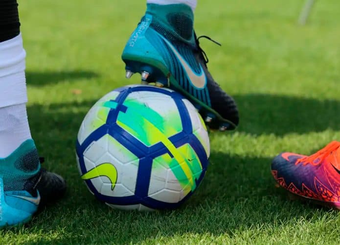 Jogador de futebol com pé sobre uma bola num campo