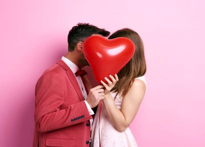 casal segurando balão de coração em foto com fundo rosa claro
