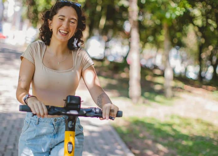 Moça sorrindo enquanto conduz uma das patinetes elétricas da Whoosh