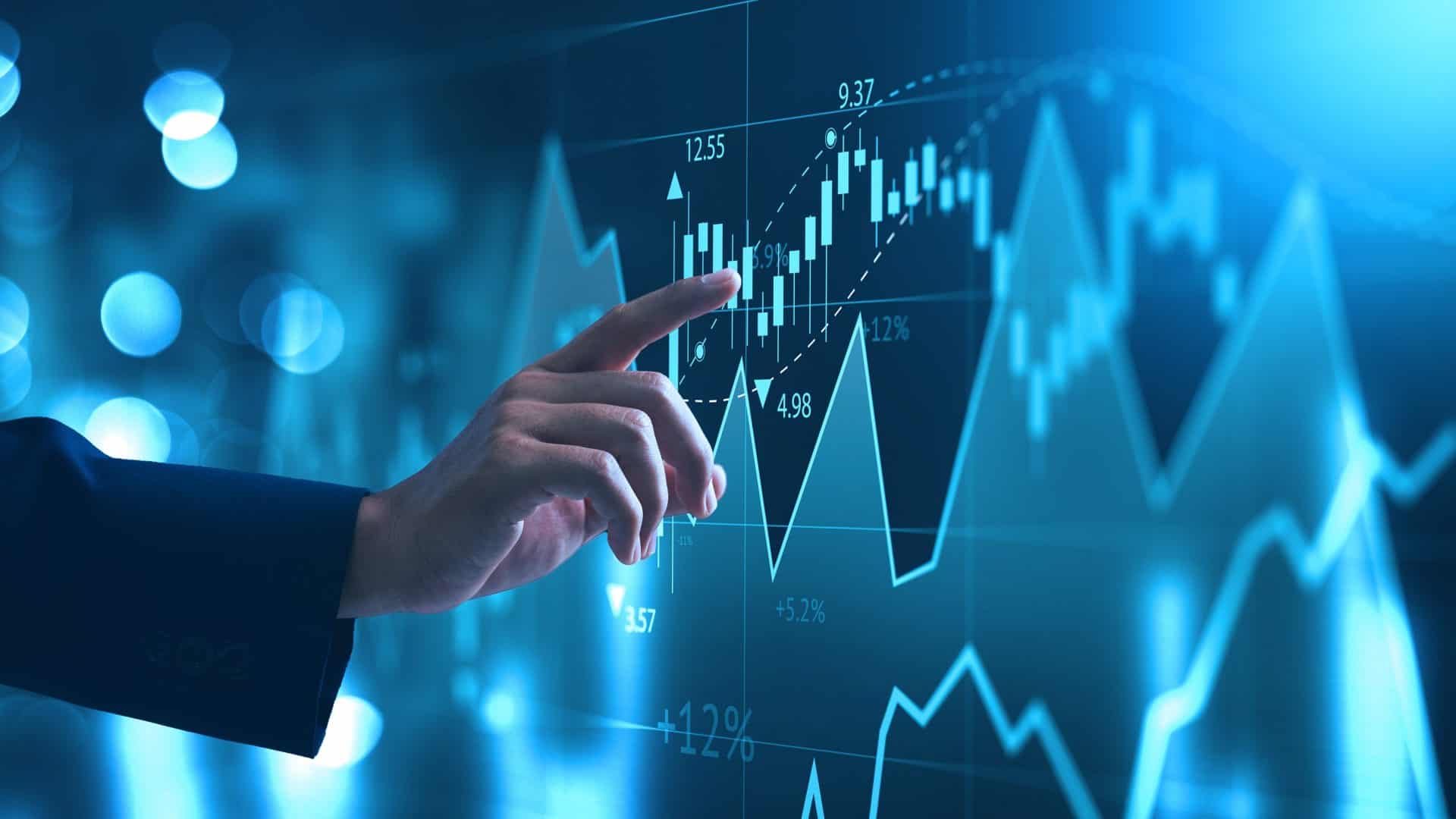 mão tocando em tela com gráficos que representam o mercado financeiro