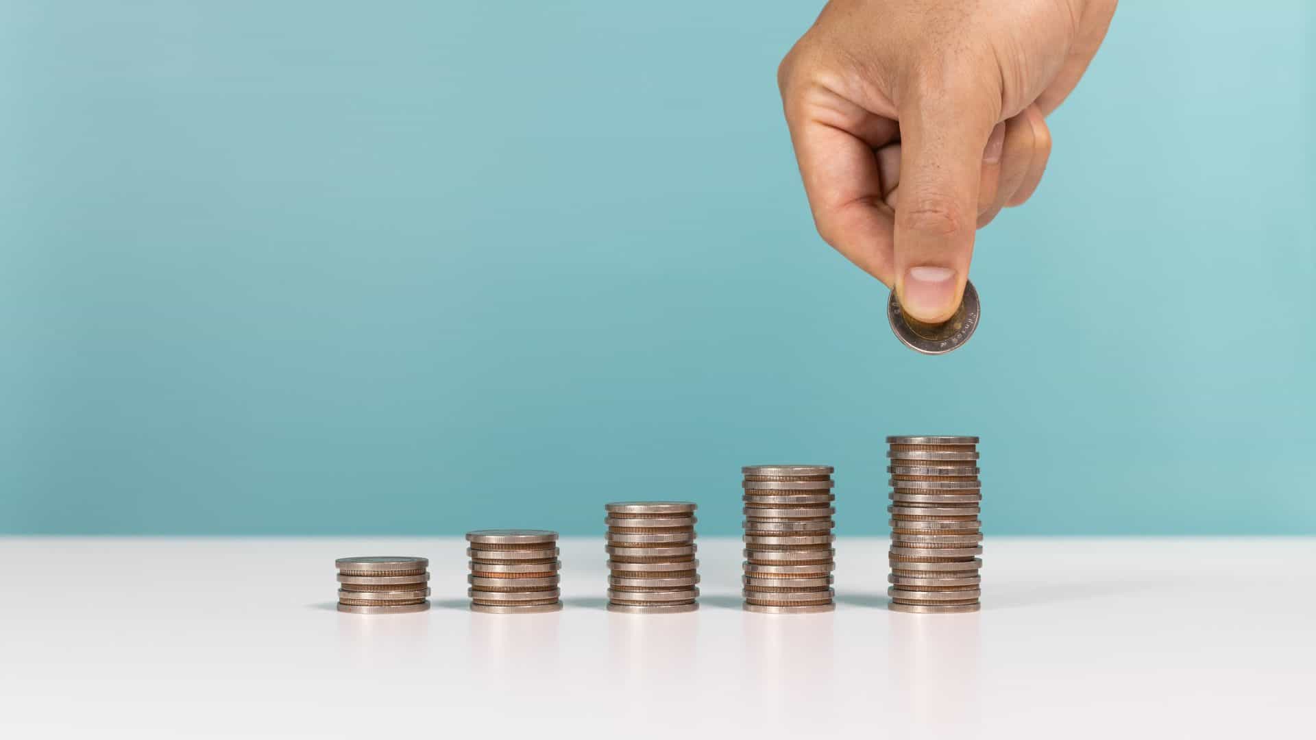 Pilhas de moedas e uma mão colocando outra em uma das pilhas