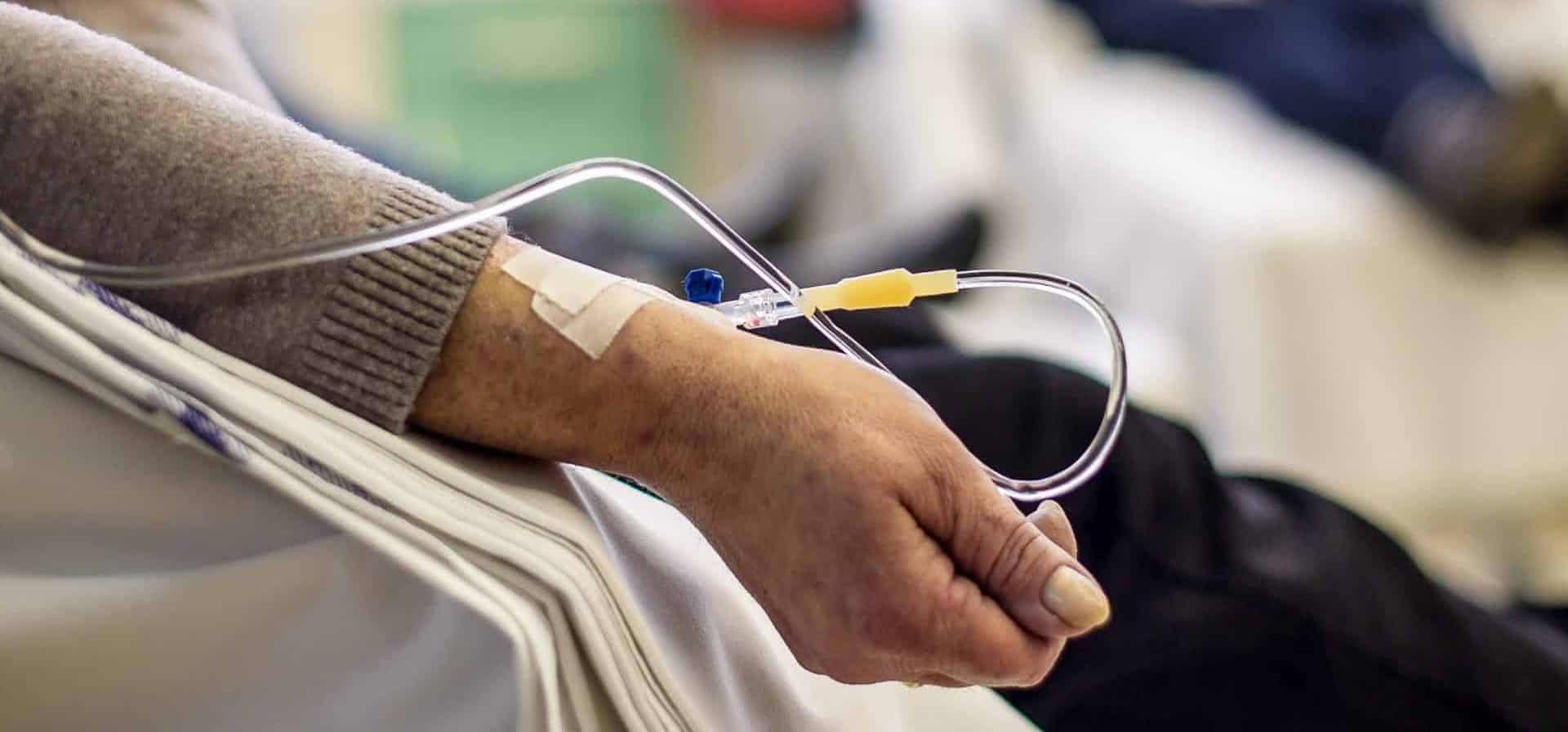 imagem mostra um paciente idoso num hospital, recebendo medicação direto na veia