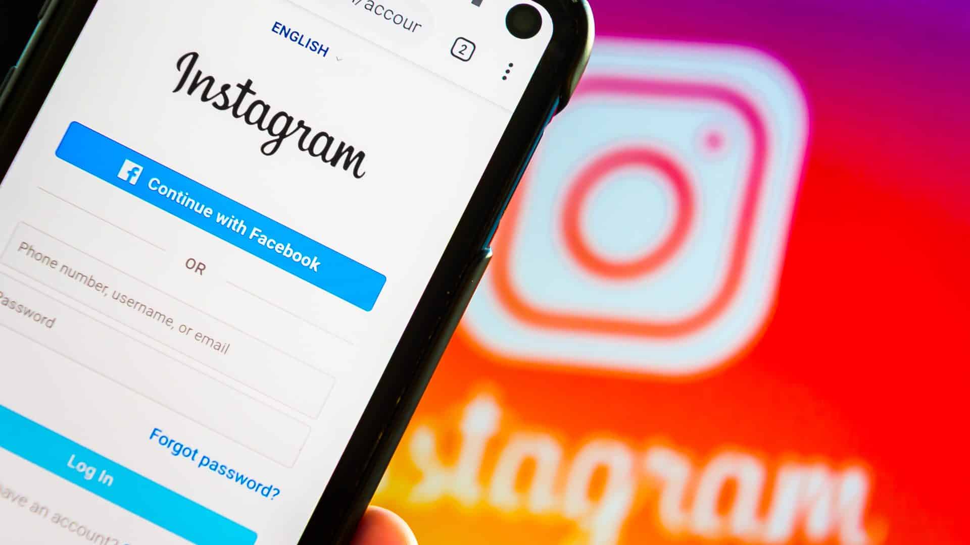 Logo do Instagram ao fundo, com página de login da rede social no plano principal em um smartphone