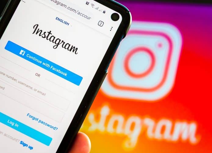 Logo do Instagram ao fundo, com página de login da rede social no plano principal em um smartphone