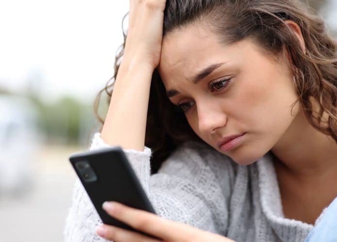 mulher com cara de triste com uma mão segurando o celular e a outra na cabeça