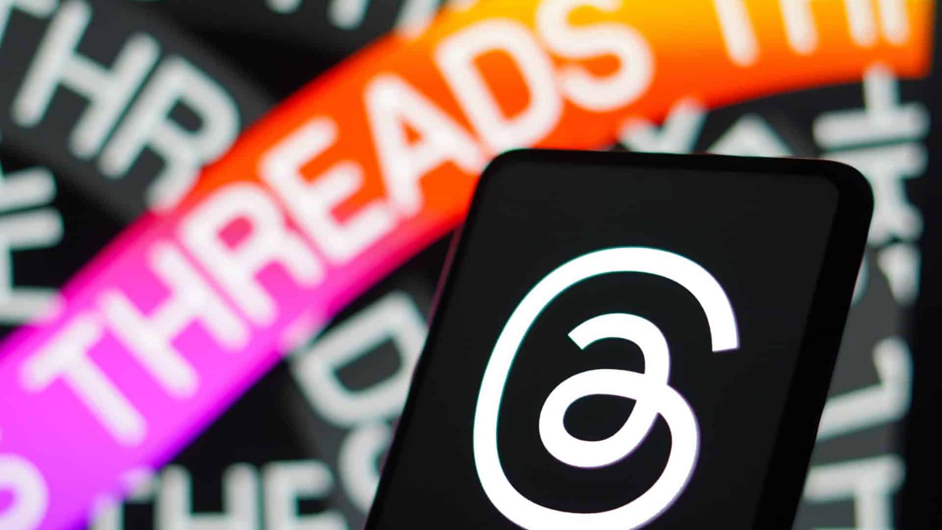 Logo do Threads exibido em tela de celular colocado na frente de monitor exibindo ilustração sobre Threads