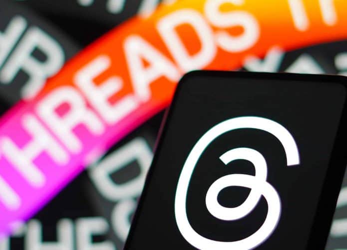 Logo do Threads exibido em tela de celular colocado na frente de monitor exibindo ilustração sobre Threads
