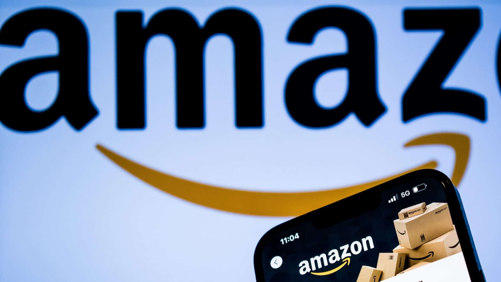 Logo grande da Aamzon, defocado no fundo, com a página da Amazon aberta, em primeiro plano, em um celular