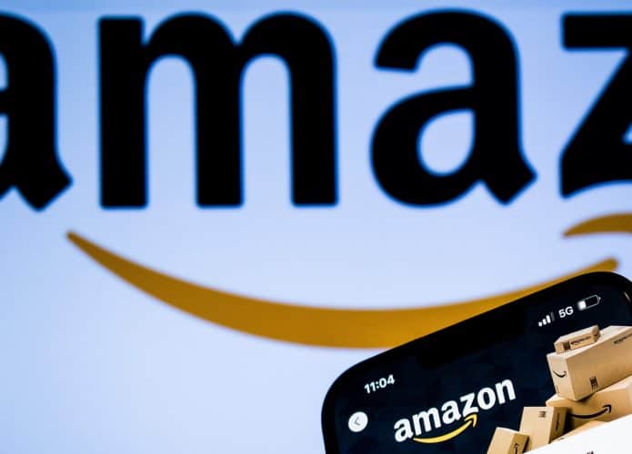 Logo grande da Aamzon, defocado no fundo, com a página da Amazon aberta, em primeiro plano, em um celular