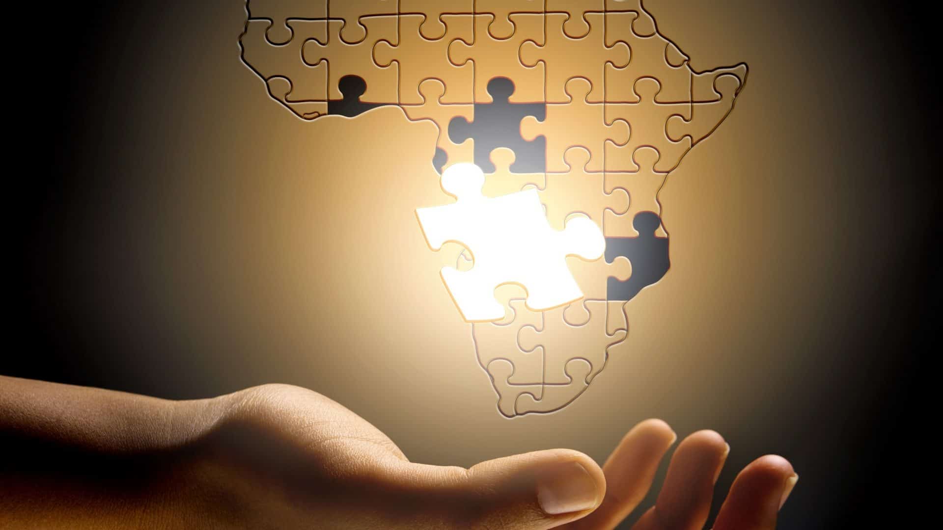 Mapa da África em formato de quebra-cabeça com uma mão humana embaixo dele
