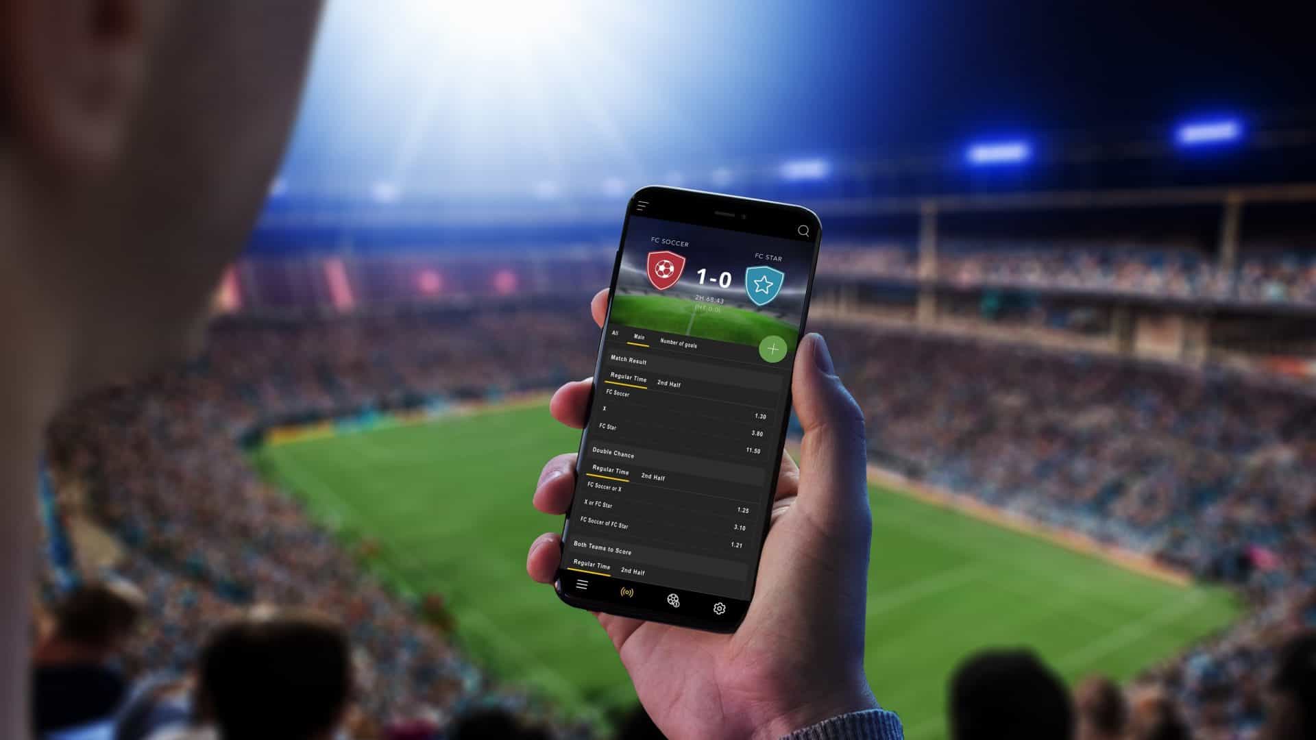 Pessoa em um estádio segurando um smartphone com uma bet na tela
