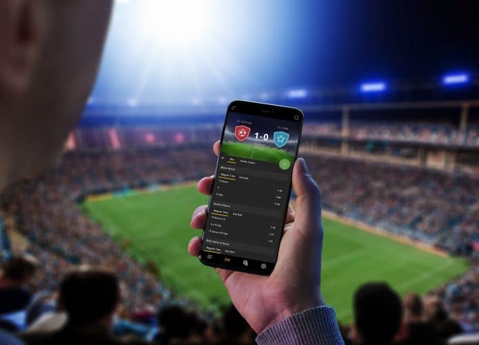 Pessoa em um estádio segurando um smartphone com uma bet na tela