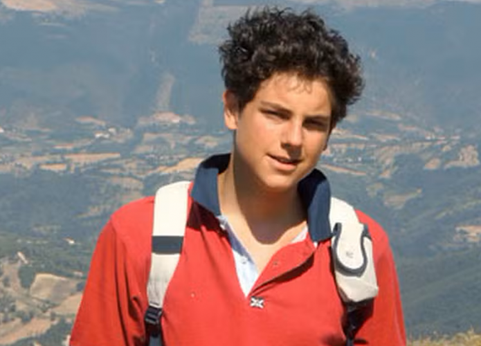 Carlo Acutis durante trilha em pico de morro com cidade ao fundo