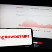 Logo da CrowdStrike em smartphone, com fundo de um monitor mostrando um gráfico no site da empresa