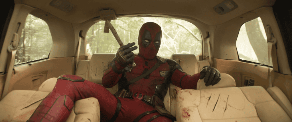Cena do filme Deadpool & Wolverine, mostrando Deadpool sentada no banco de trás de uma carro, segurando um martelo e com o uniforme ensanguentado