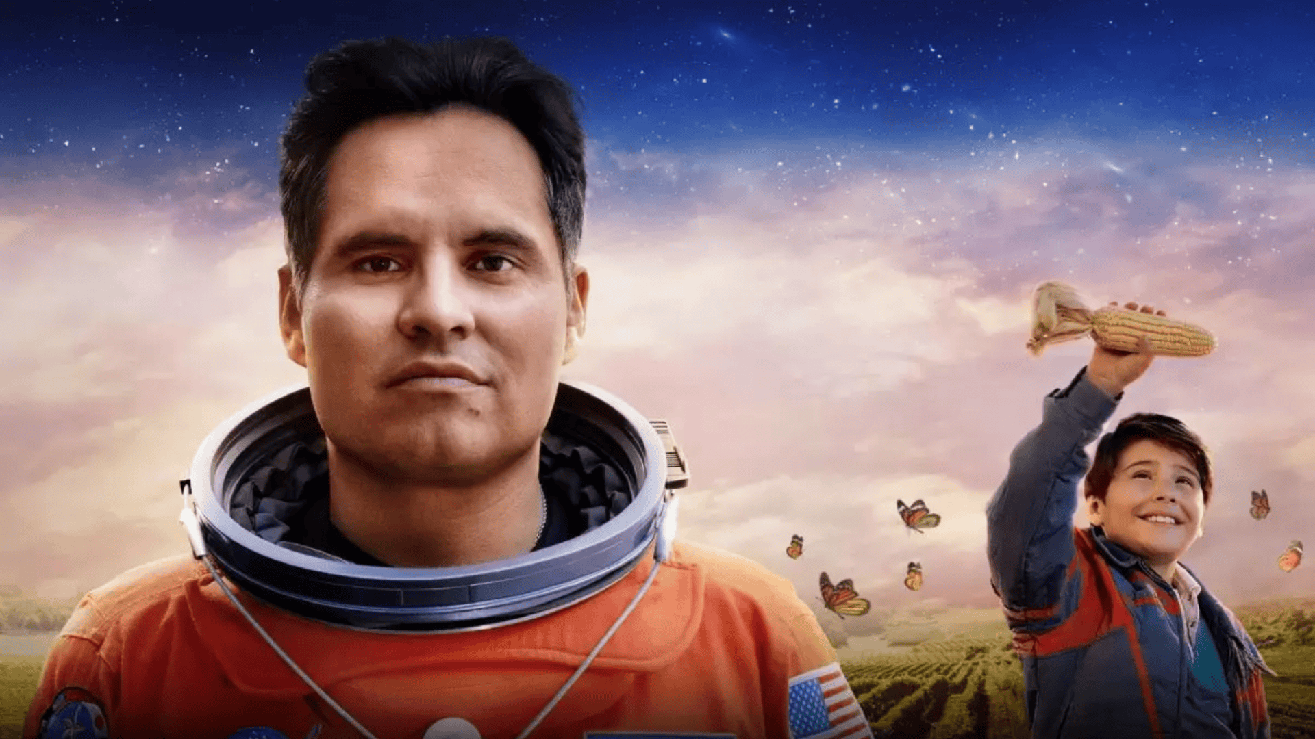 Imagem mostra um astronauta em destaque em uma roupa espacial laranja e um menino no fundo em uma lavoura de milho
