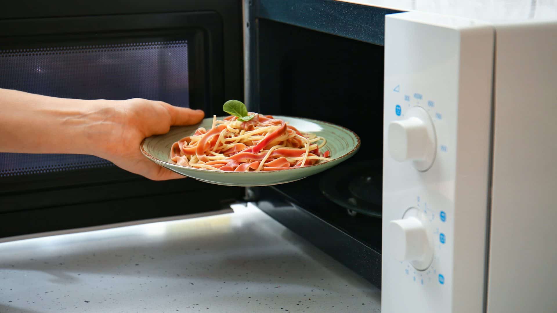 Pessoa levando prato de macarronada para aquecer no micro-ondas