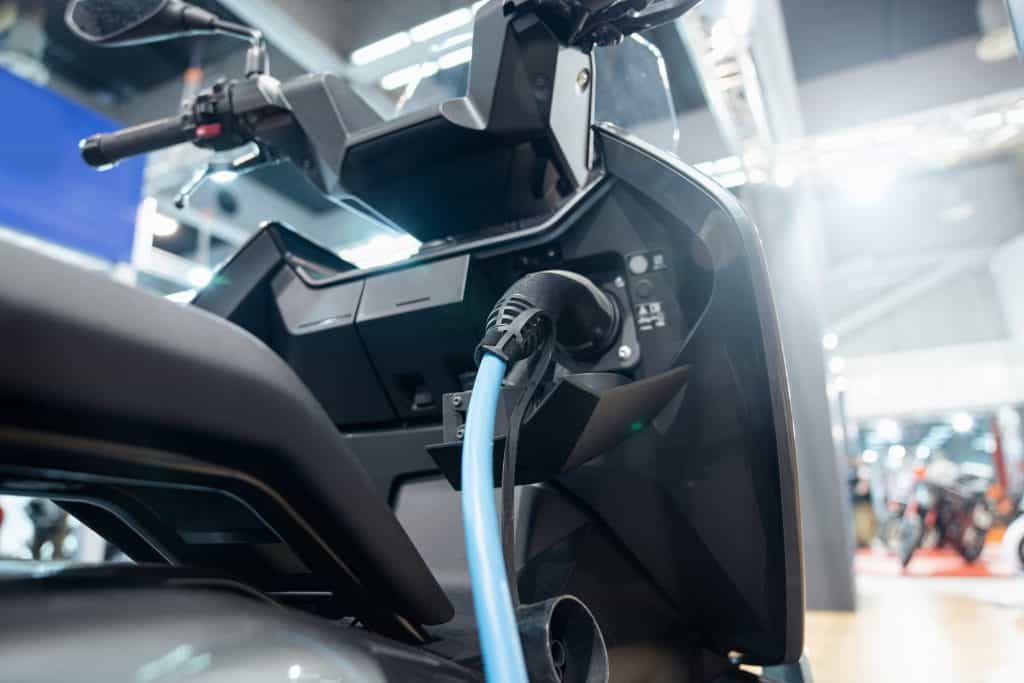 Imagem mostra uma moto elétrica conectada a um carregador, em uma estação de carregamento