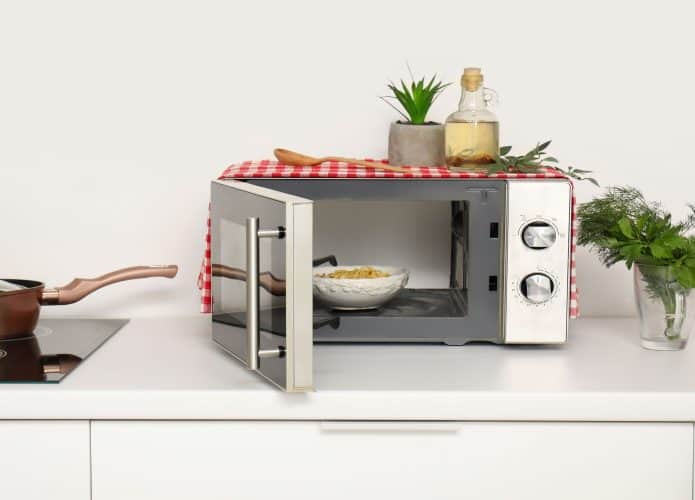 Tigela com macarrão no micro-ondas moderno em bancada branca da cozinha.