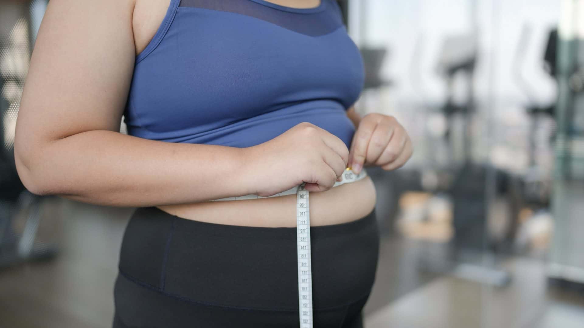 Imagem mostra uma mulher com uma fita métrica ao redor da barriga.