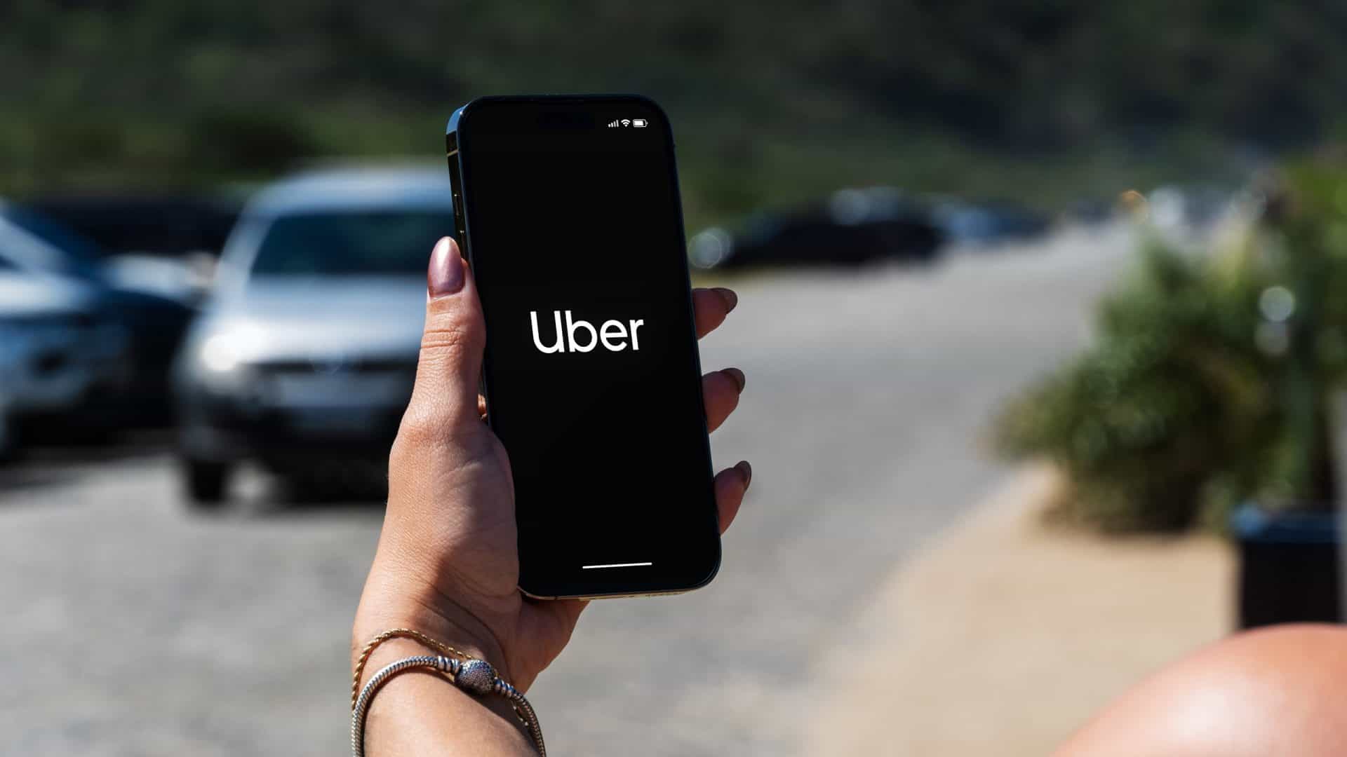Mão de uma pessoa segurando um celular. Nele aparece o logo da Uber