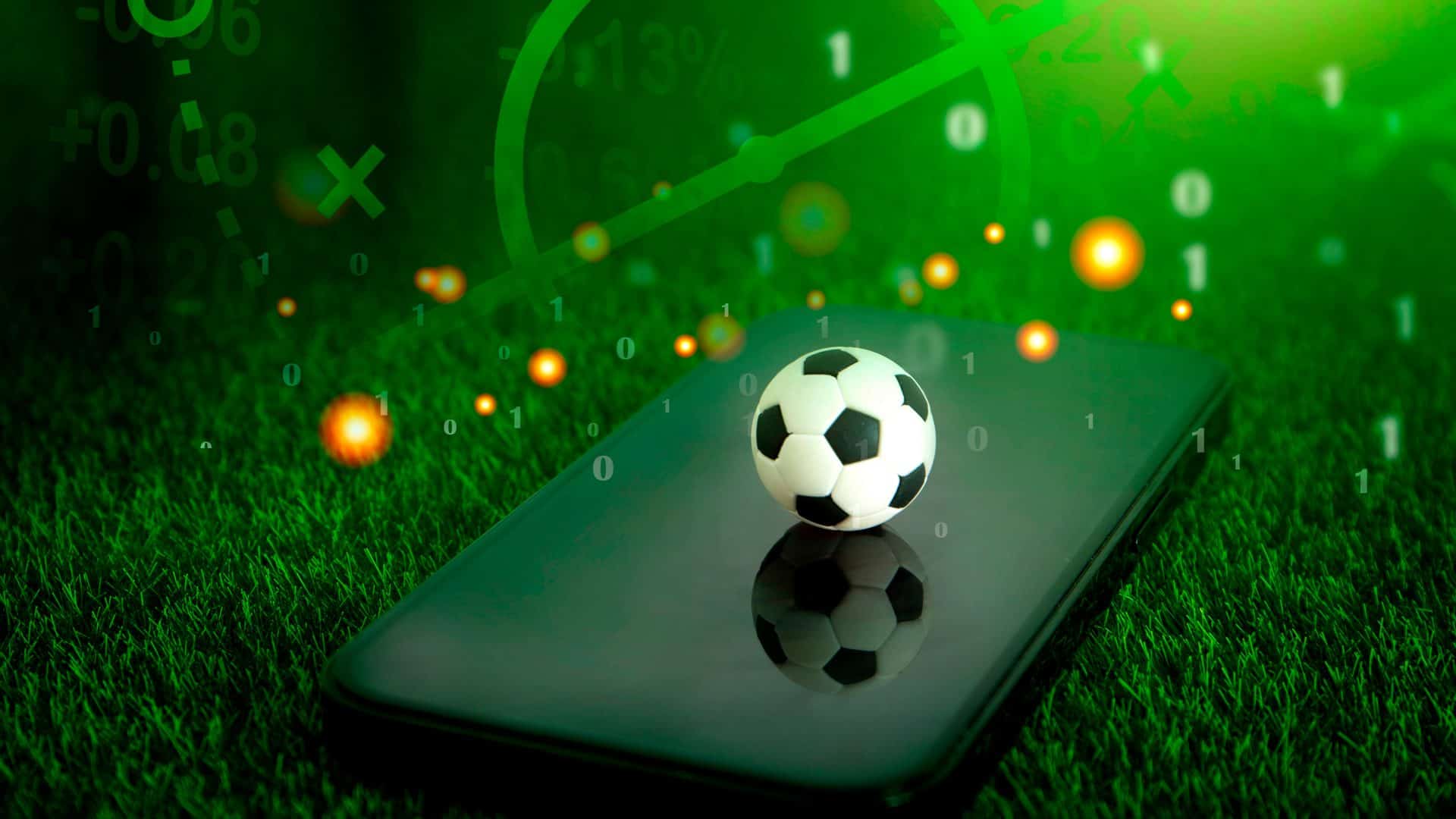 Montagem com bola de futebol em cima de celular num campo de futebol